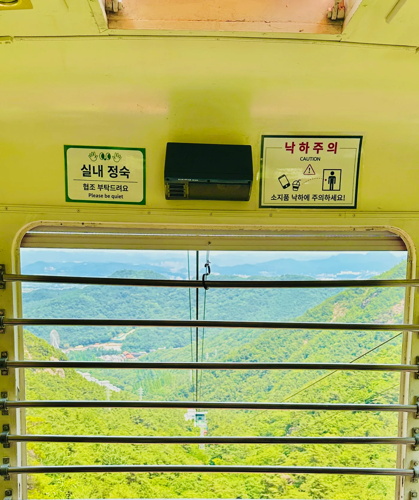 칸 안에서 본 열린 창과 쇠막대 너머의 초록 산골짜기, 먼 시가지