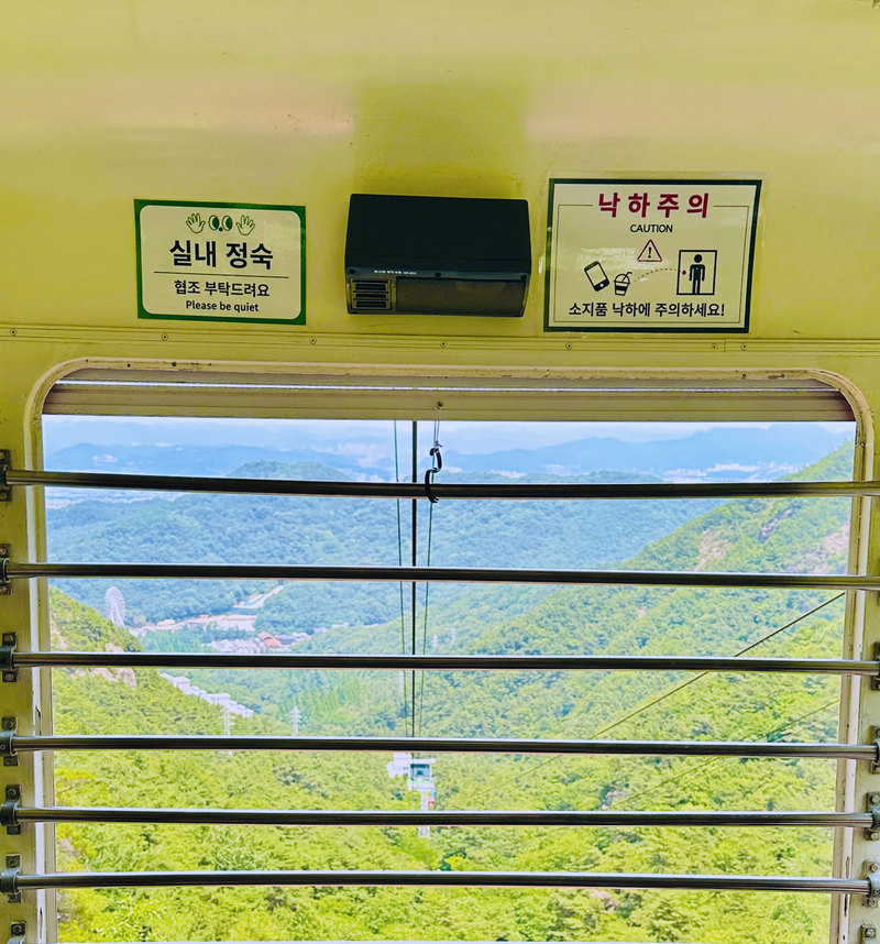 칸 안에서 본 열린 창과 쇠막대 너머의 초록 산골짜기, 먼 시가지